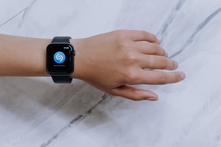 Close-up of a smartwatch on a wrist showing a music identification app with a marble background.