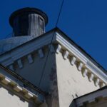 Low angle shot of building roof and dome under a bright blue sky, showcasing architectural detail.