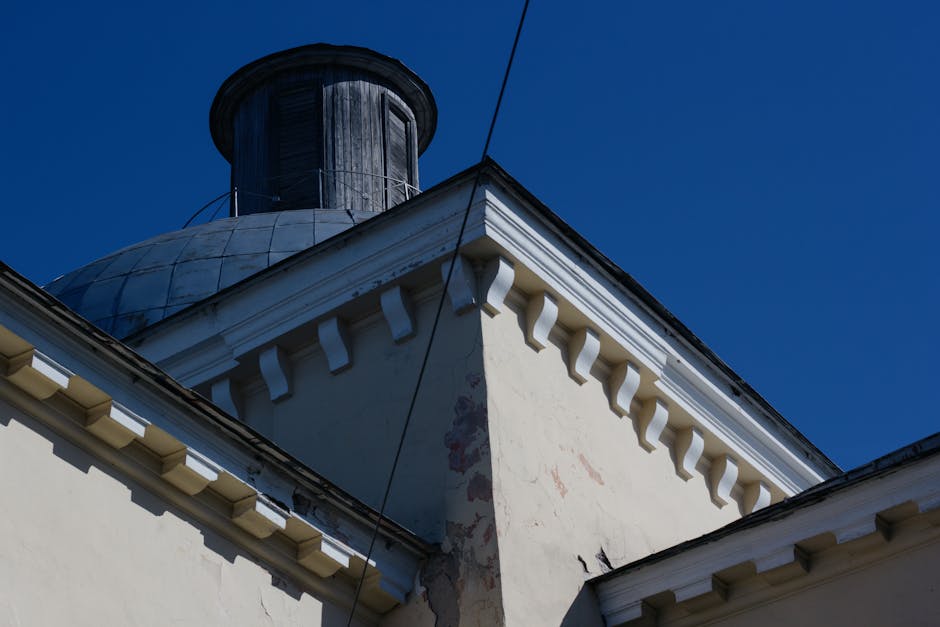 Low angle shot of building roof and dome under a bright blue sky, showcasing architectural detail.