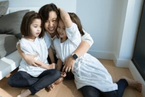 A joyful mother embraces her two daughters indoors, capturing a heartwarming family moment.