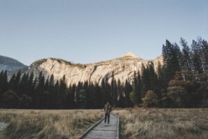 A man walks alone on a wooden pathway in Yosemite Valley surrounded by mountains and trees.