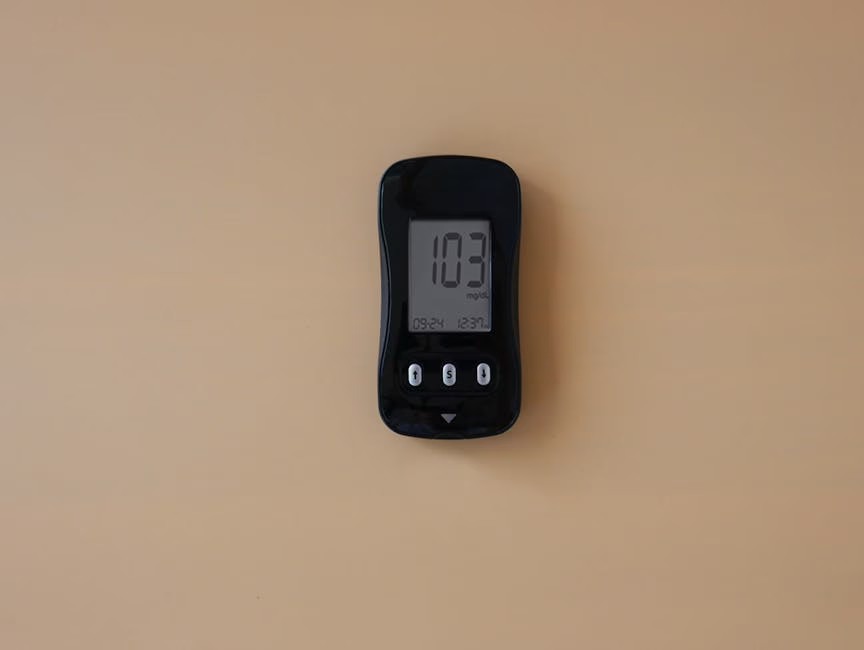 Close-up of a blood glucose meter displaying 103 mg/dL on beige surface.